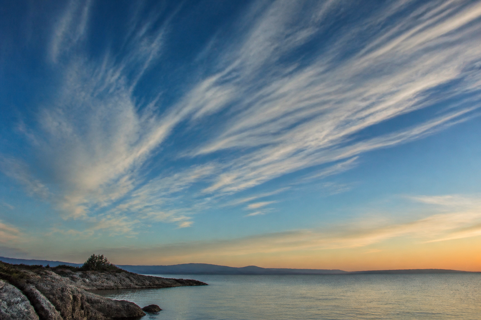 Longues bandes de cirrus fibreux étirées par le vent d'altitude dans un ciel bleu pâle
