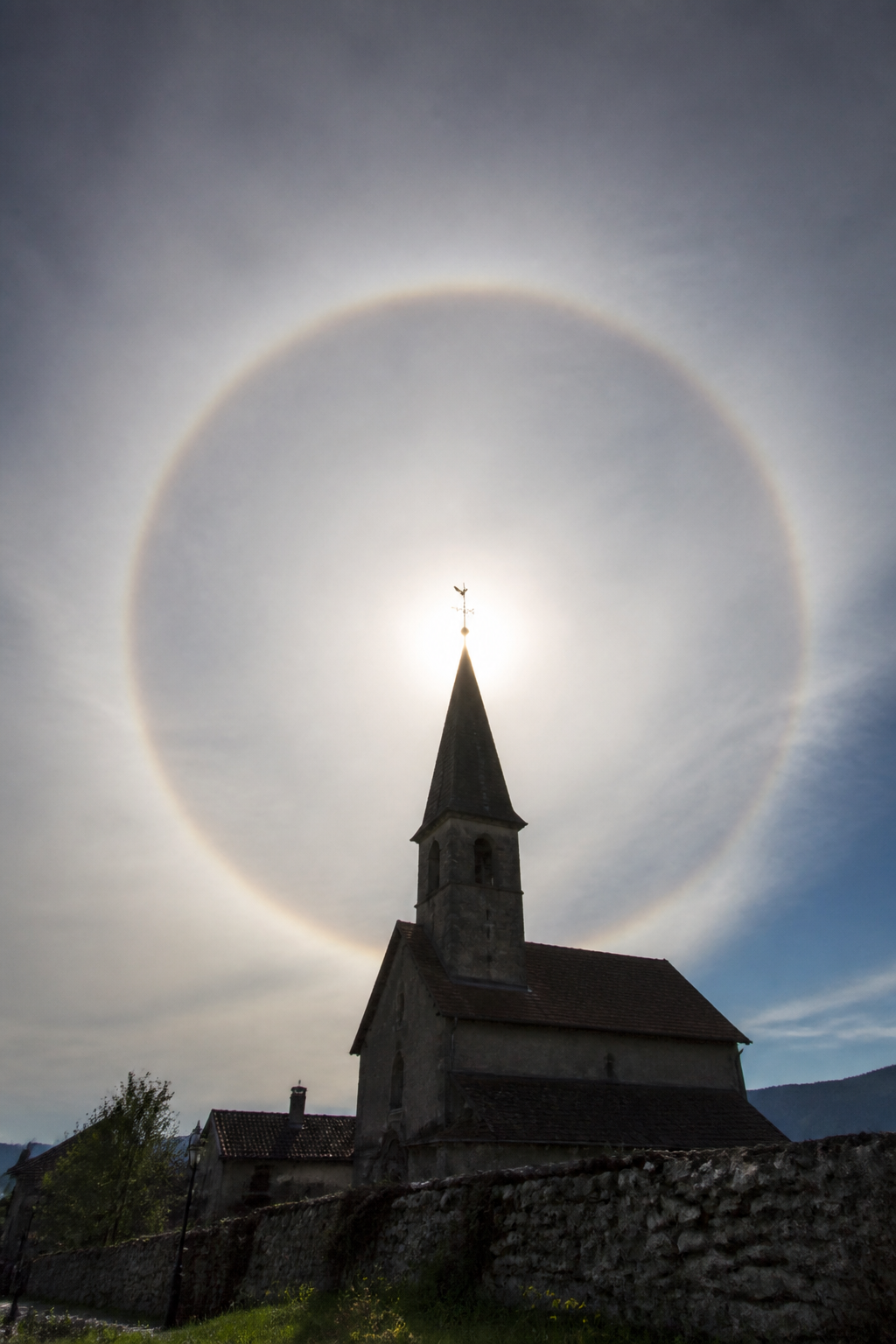 Halo circulaire complet autour du soleil masqué par un clocher, dans un voile de cirrostratus