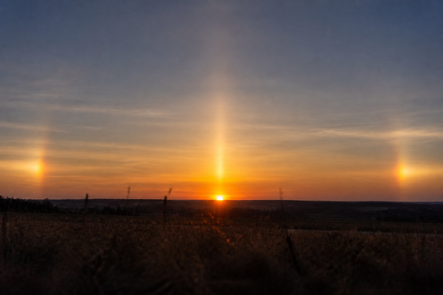 Pilier solaire orangé dressé verticalement au-dessus du soleil couchant, au ras d'un horizon dégagé